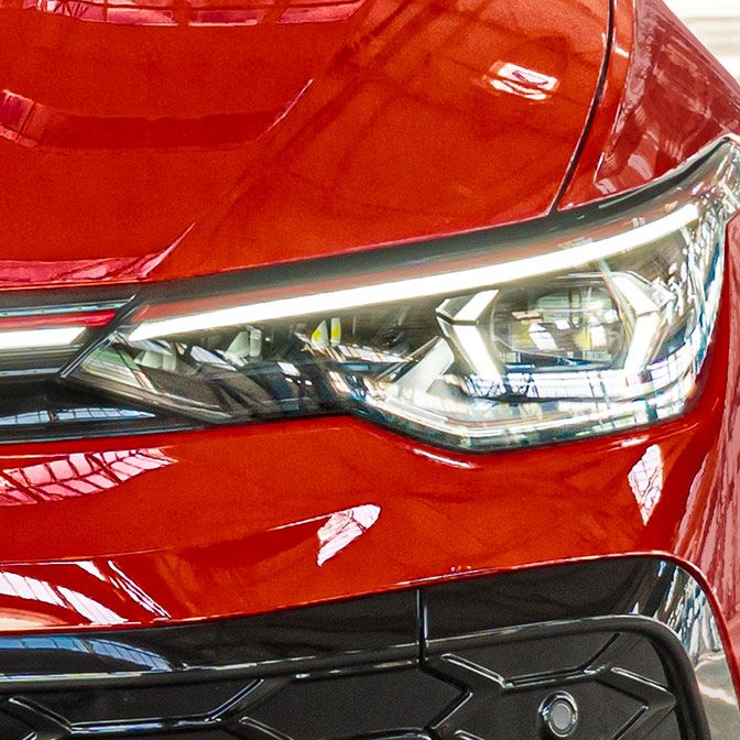 Nahaufnahme eines roten Golf GTI, die sich auf einen Frontscheinwerfer konzentriert. Die Oberfläche ist glänzend und reflektiert das Licht. Der Scheinwerfer hat ein modernes, scharfkantiges Design.