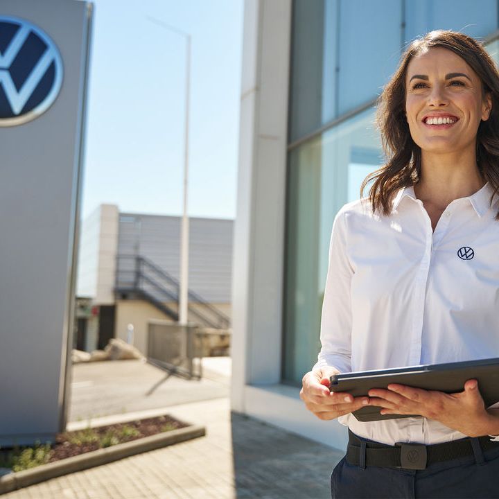 Жена с корпоративно облекло на Volkswagen държи в ръце таблед пред сервизен комплекс на марката.