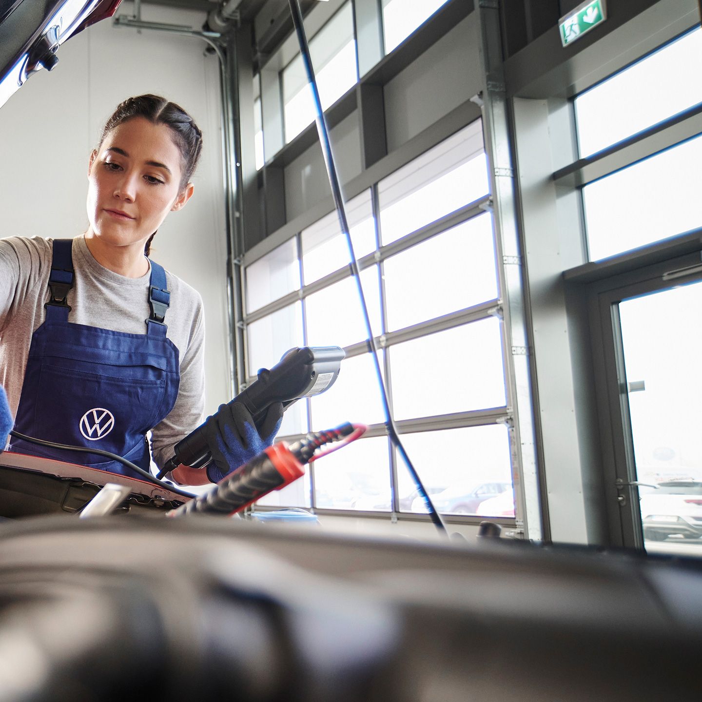 Механик на Volkswagen извършва проверка под капака на автомобил в сервиз.