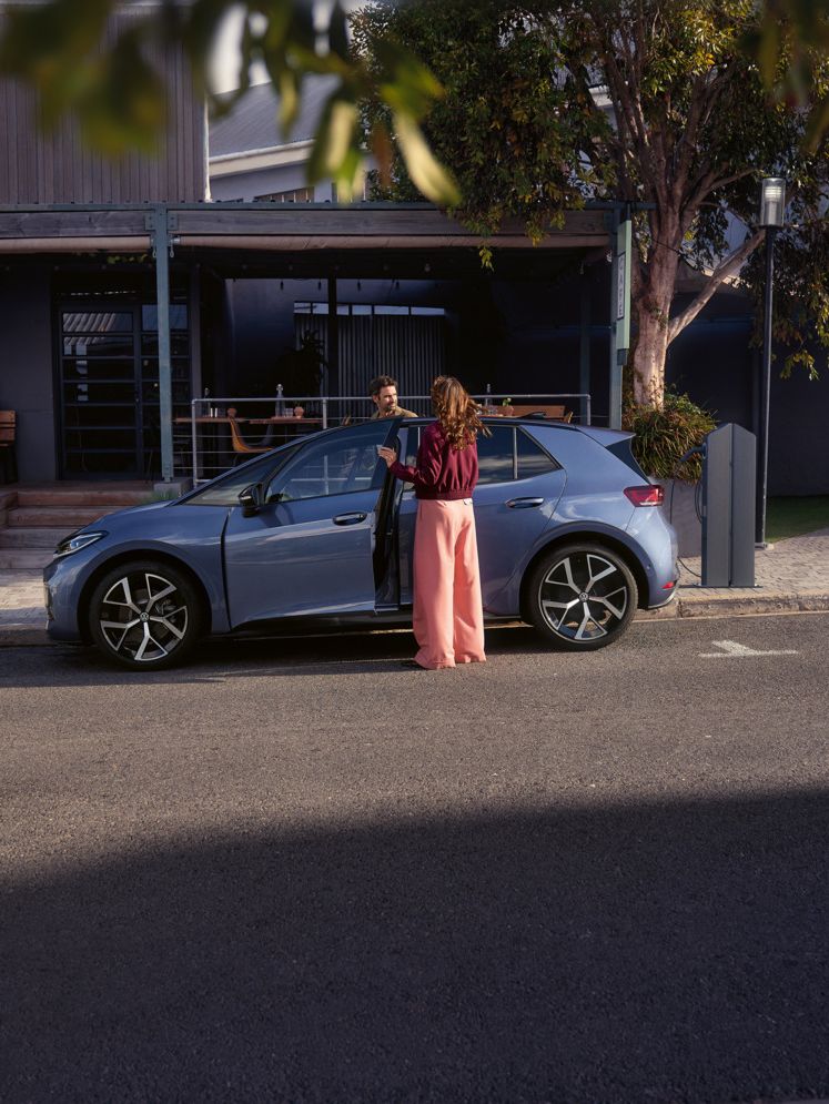 Жена и мъж се качват в син VW ID.3 Neo, паркиран пред кафене
