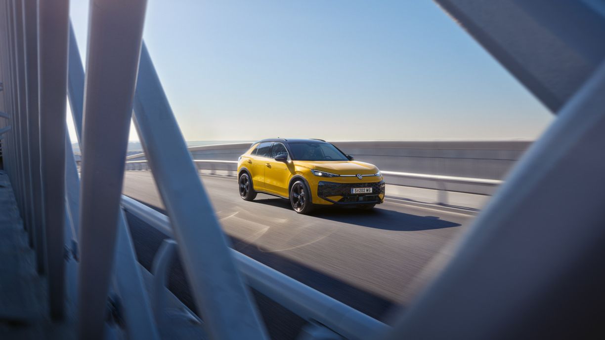Жълт Volkswagen T-Roc в движение по мост при слънчево време