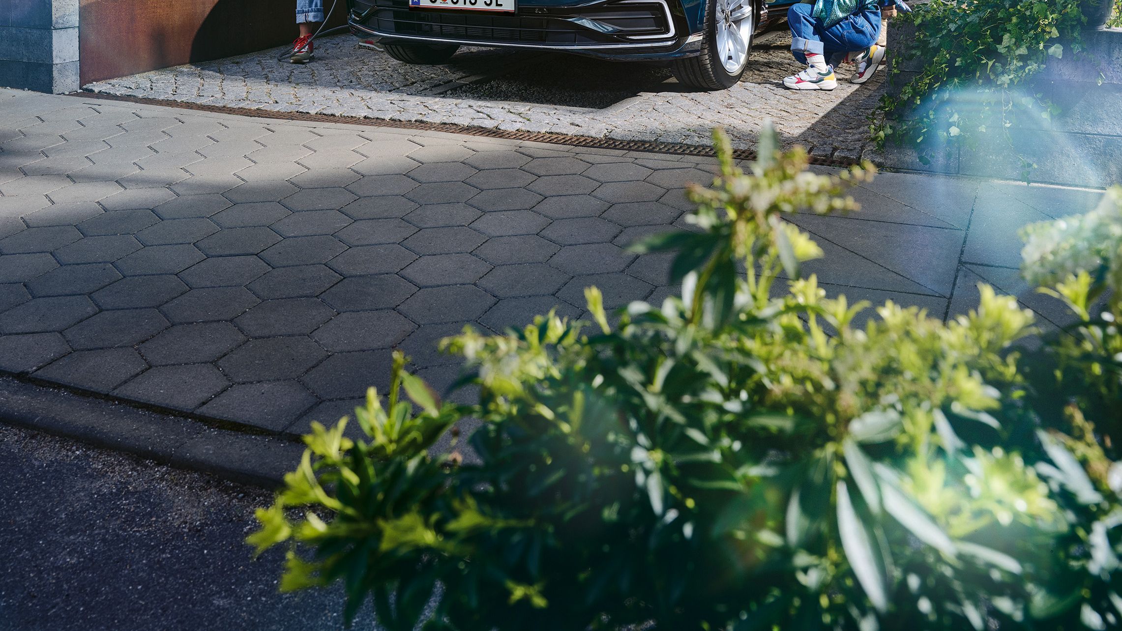 Ein junges Paar spielt mit der kleinen Tochter rund um den in der Einfahrt parkenden VW Passat GTE Variant.
