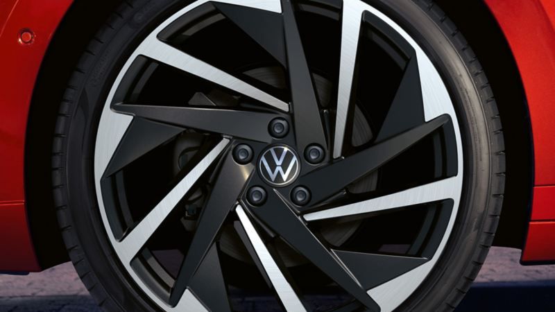 Близък план на тъмносивa алуминиева джанта с емблема Volkswagen на червен Arteon Shooting Brake