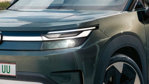 Зелен VW ID. Cross стои пред модерна стъклена сграда върху бетонна повърхност.