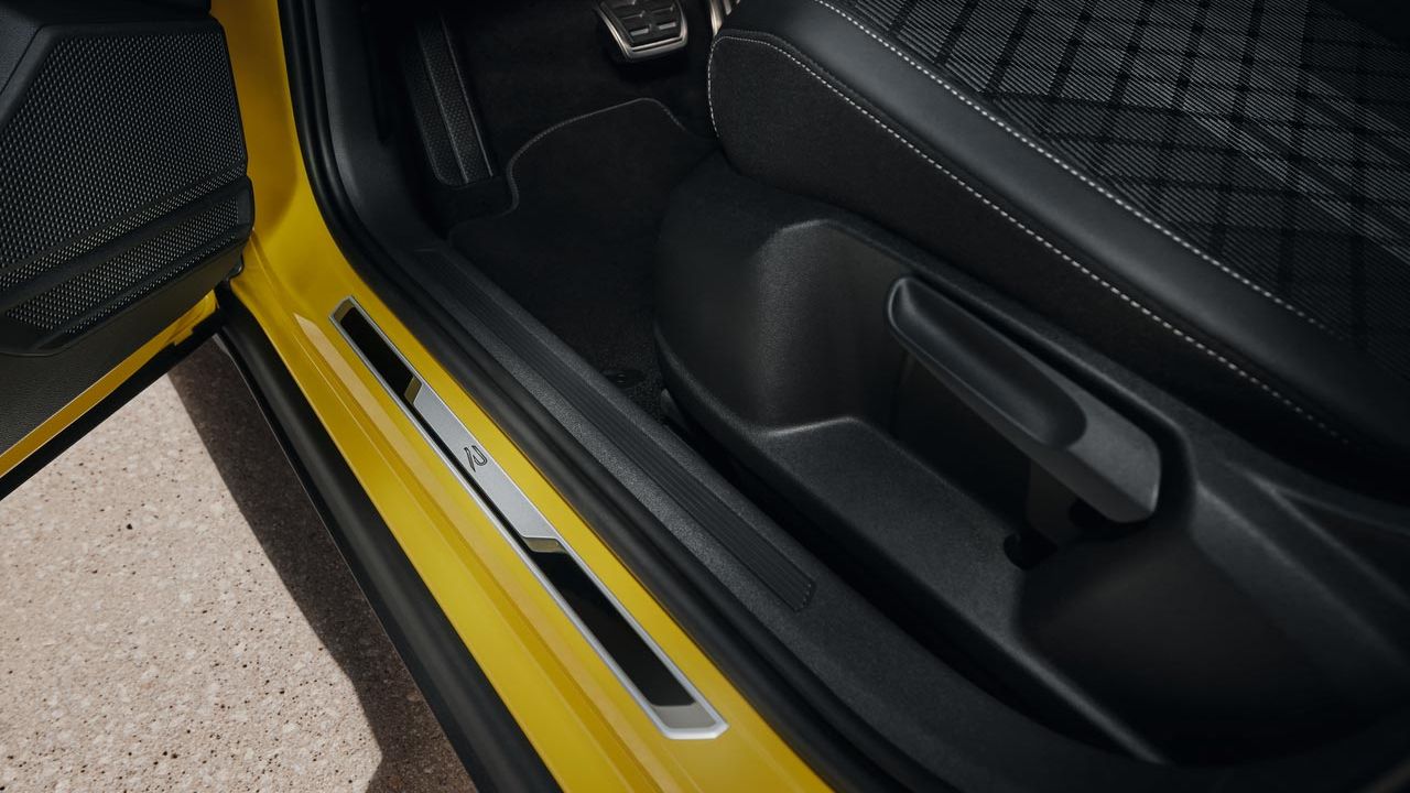 Изглед към долната част на седалката на водача в жълт VW T-Cross с отворена предна врата и панел от четкана неръждаема стомана на прага на вратата.