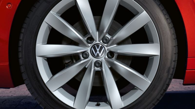 Близък план на сребриста алуминиева джанта с емблема Volkswagen на червен Arteon Shooting Brake
