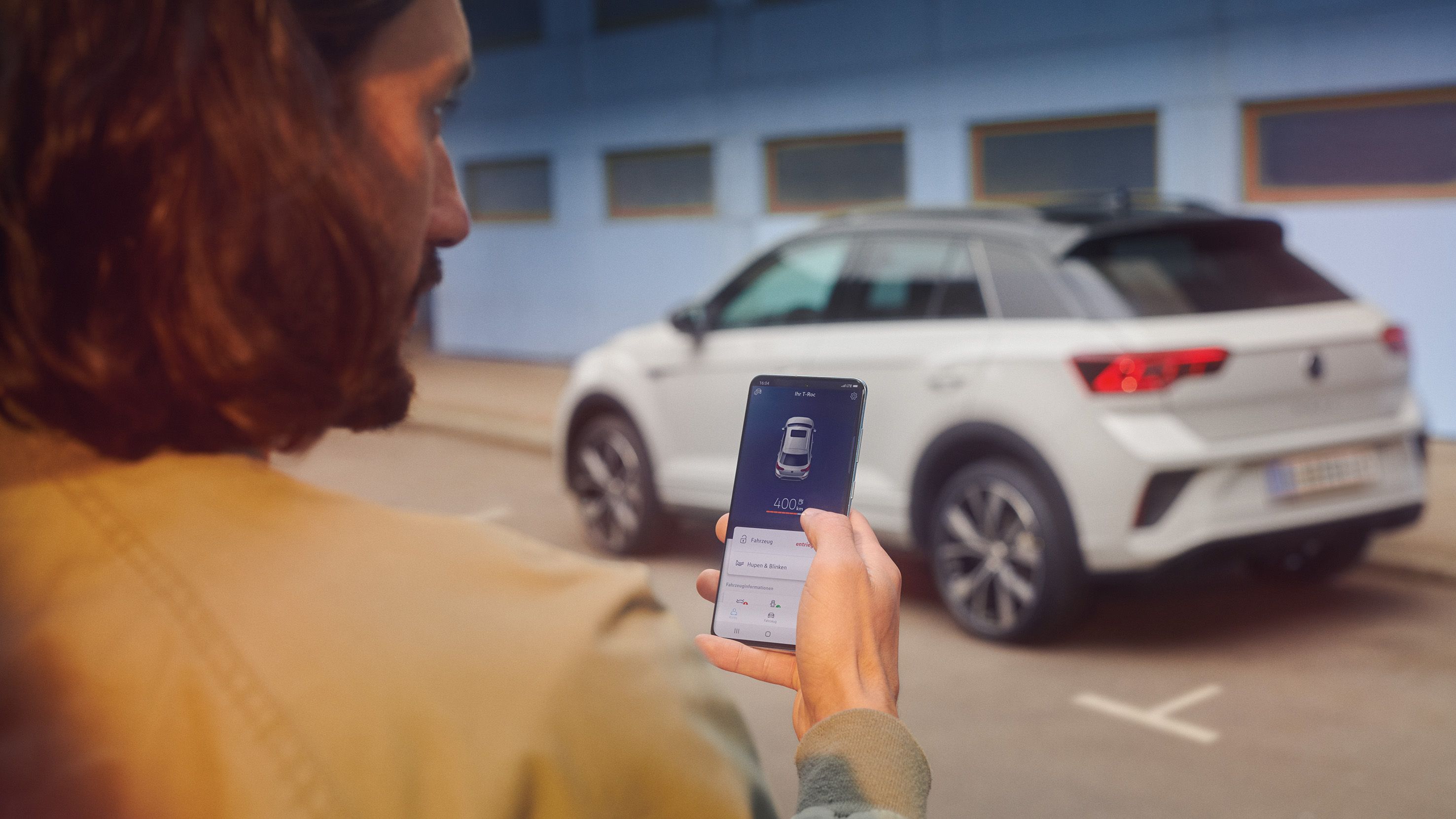 VW T-Roc R-Line в бял цвят, спрян пред сграда, поглед отстрани, мъж със смартфон на преден план