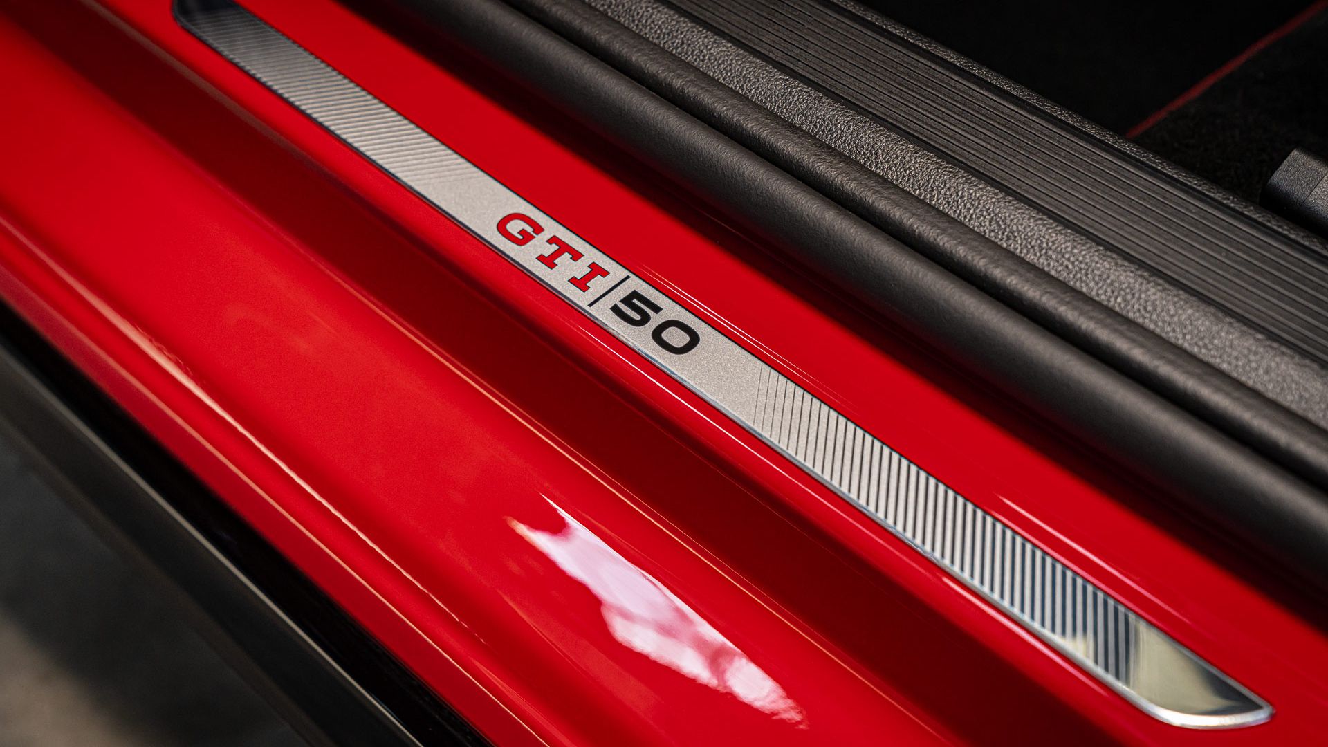 Nahaufnahme der Türschwelle eines roten Golf GTI mit einer silbernen Plakette. Auf der Plakette steht "GTI 50". Das Bild zeigt die Detailarbeit und die sportliche Ausführung des Autos.