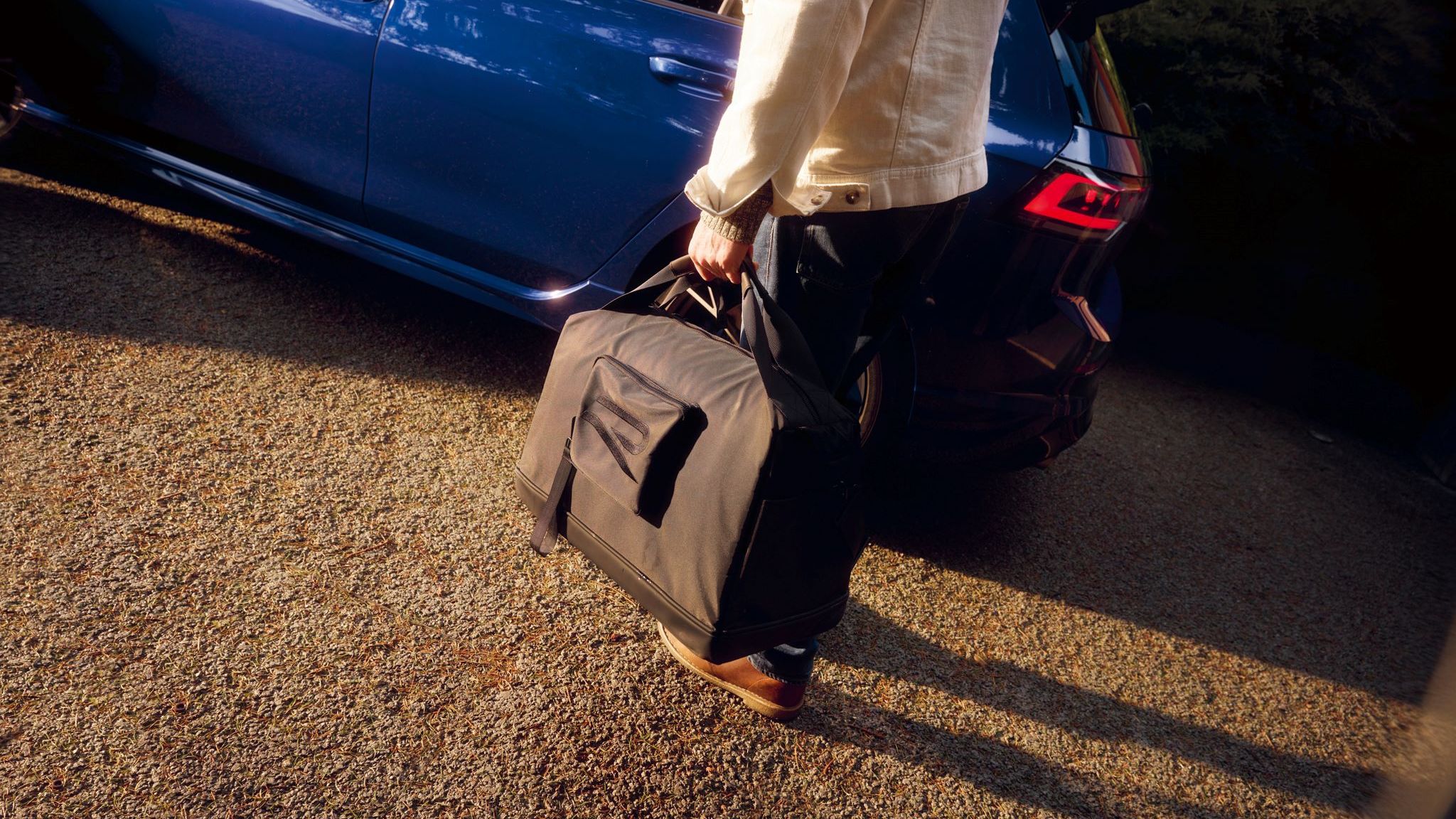 Person hat eine Tragetasche mit R-Logo in der Hand und steht vor einem Golf R.