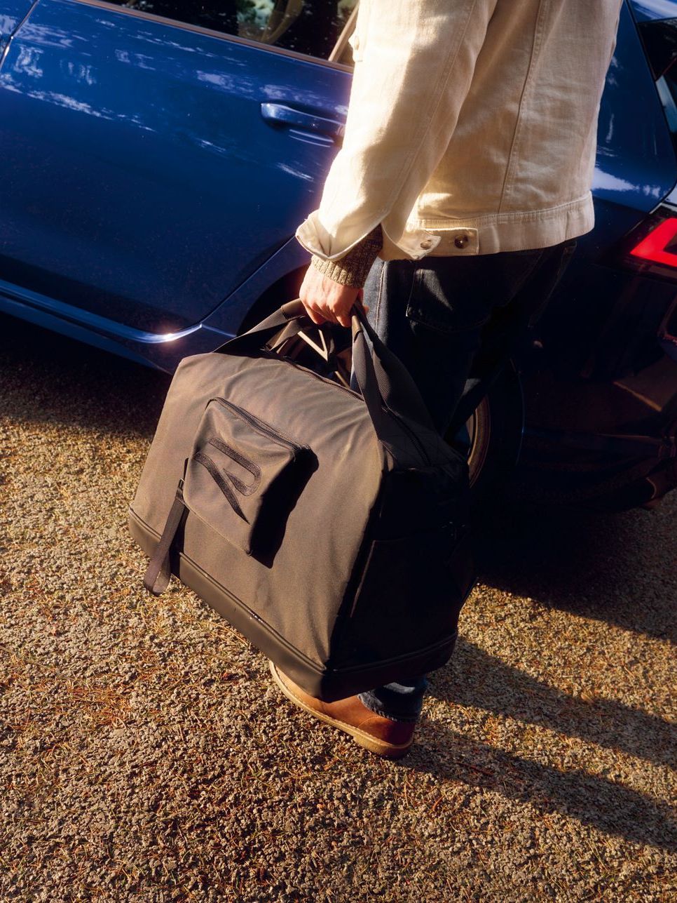 Person hat eine Tragetasche mit R-Logo in der Hand und steht vor einem Golf R.