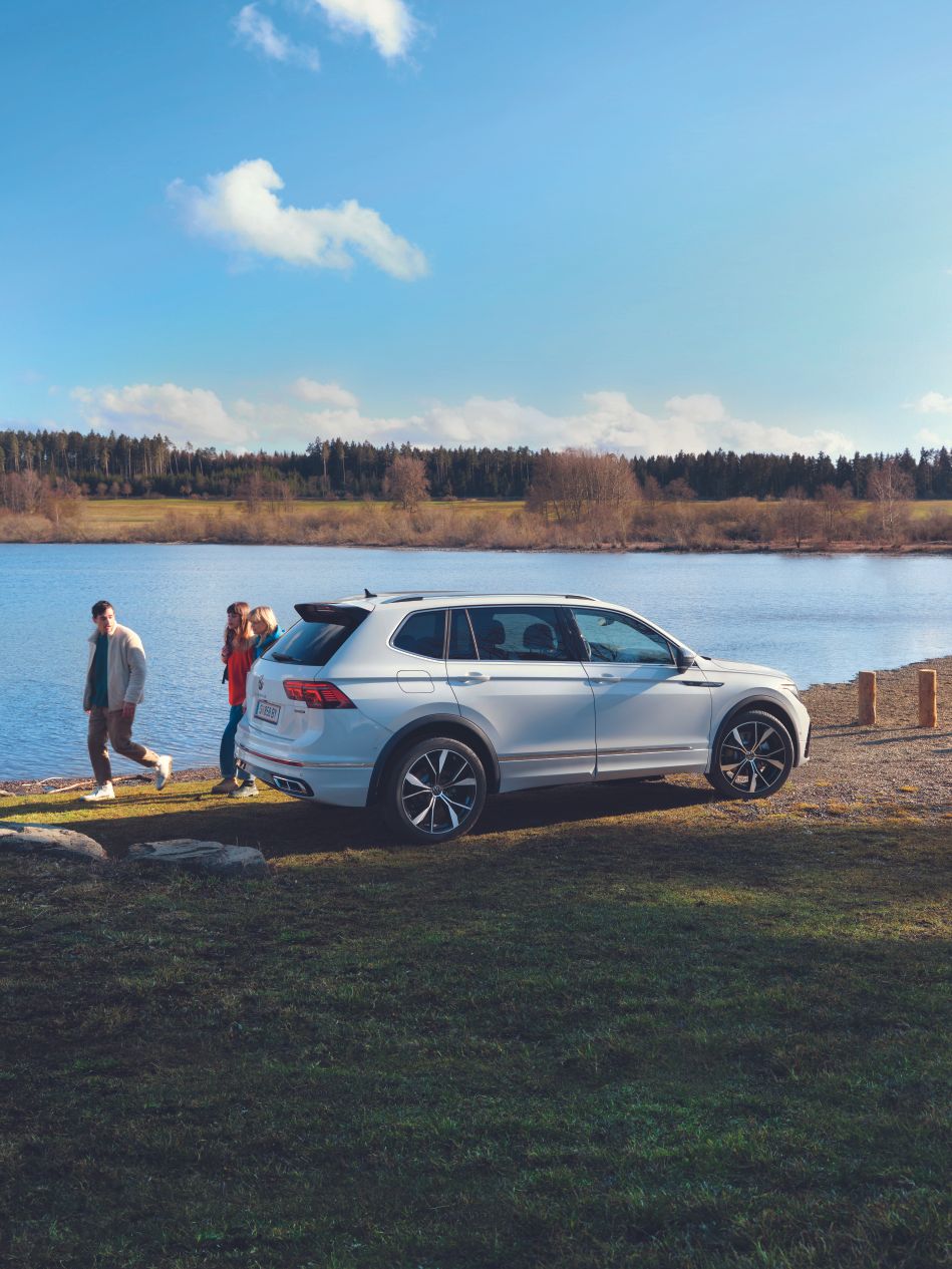 VW Tiguan Allspace е паркиран до езеро, зад него минават трима души