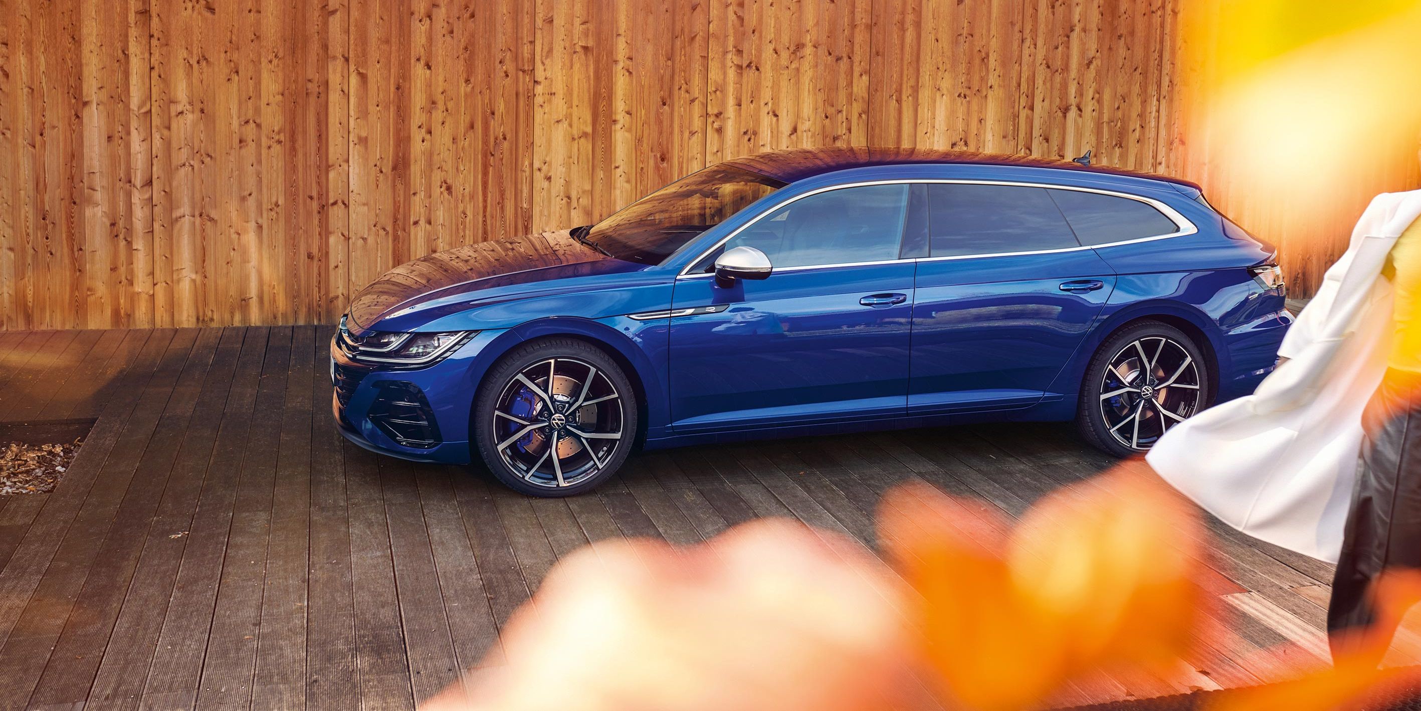 Елегантен син Volkswagen Arteon Shooting Brake паркиран пред модерна дървена сграда с есенни акценти