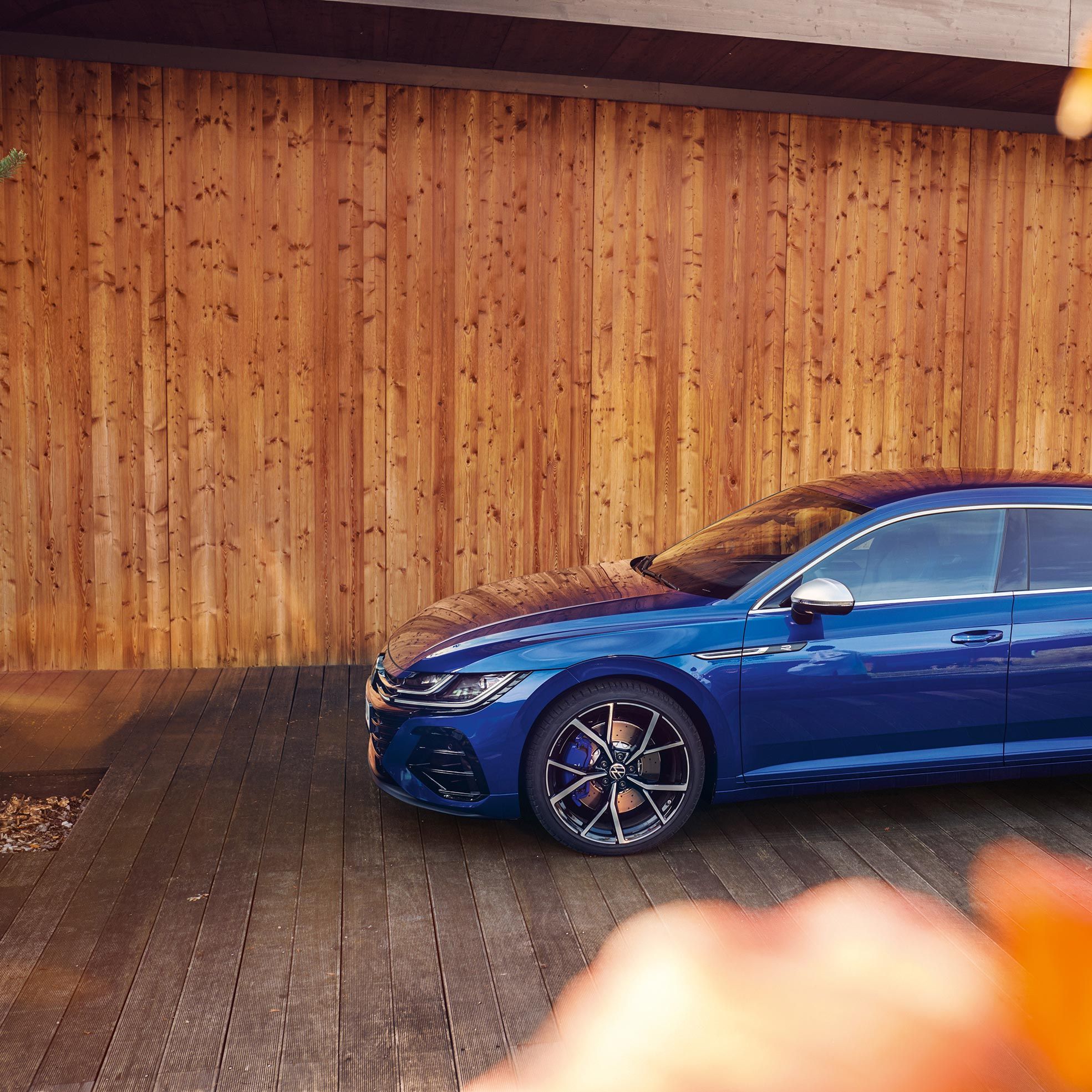 Елегантен син Volkswagen Arteon Shooting Brake паркиран пред модерна дървена сграда с есенни акценти