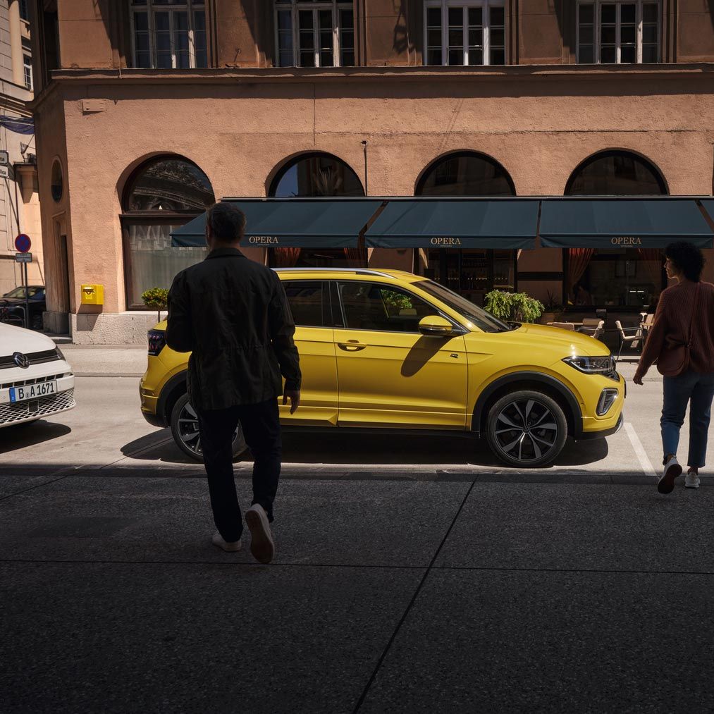 Мъж и жена се приближават до жълт VW T-Cross отстрани на пътя.