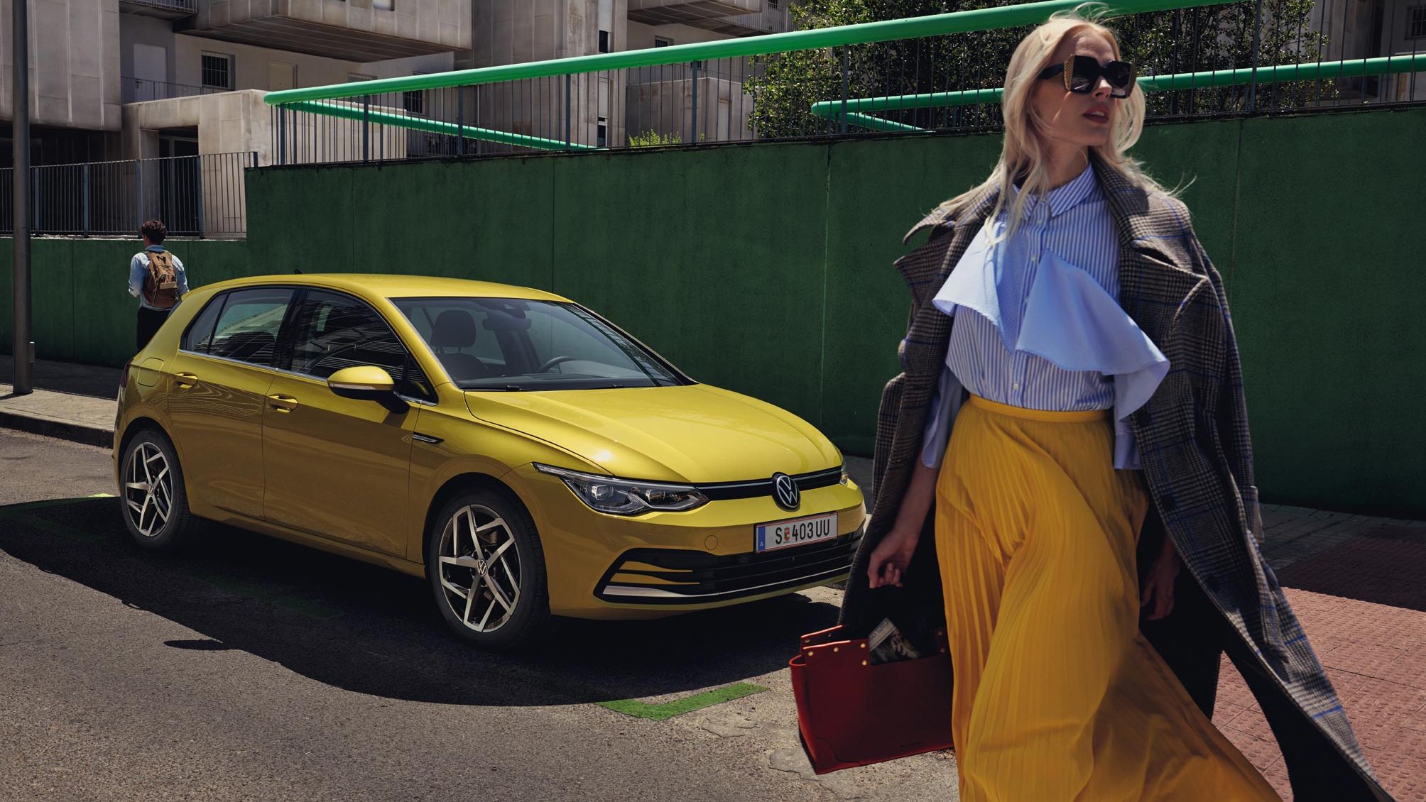 Жълт Volkswagen Golf паркиран на градска улица с модерно облечена жена на преден план