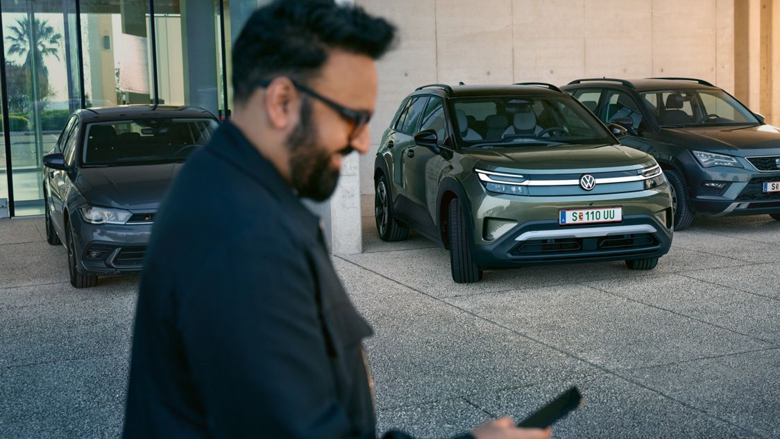 Мъж гледа смартфона си, на заден план има VW ID. Cross автоматично влиза в паркомясто.