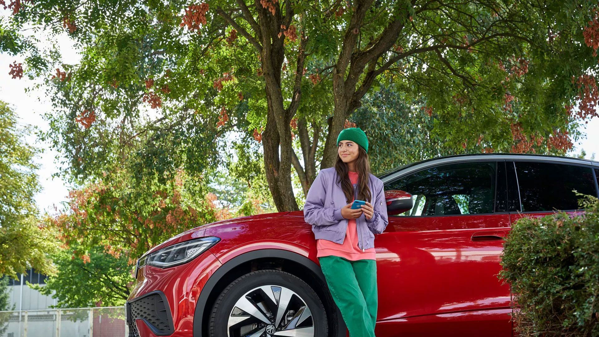 Една жена се обляга на червен VW ID.