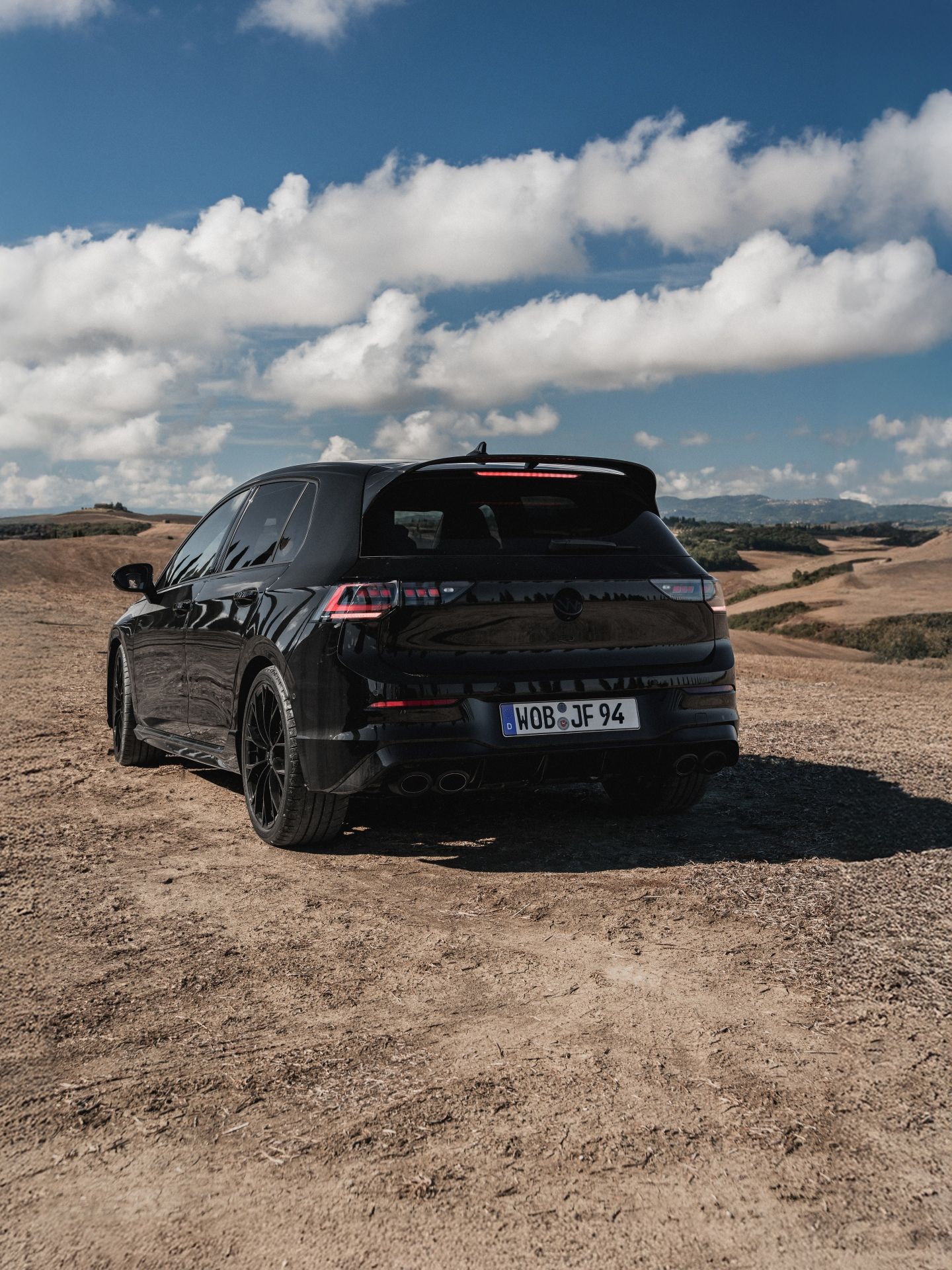 Черен Volkswagen Golf R, заснет отзад сред живописен пейзаж с хълмове и синьо небе
