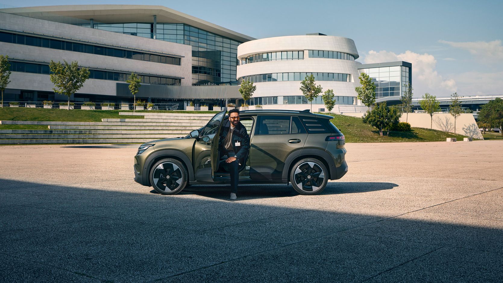 Мъж излиза през шофьорската врата на VW ID. Cross, който стои пред модерна многоетажна сграда на компанията.