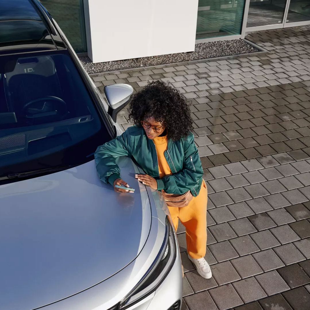 Поглед отгоре на VW ID., жена се е облегнала на предния капак