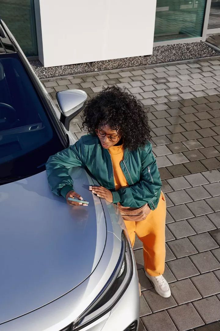 Поглед отгоре на VW ID., жена се е облегнала на предния капак