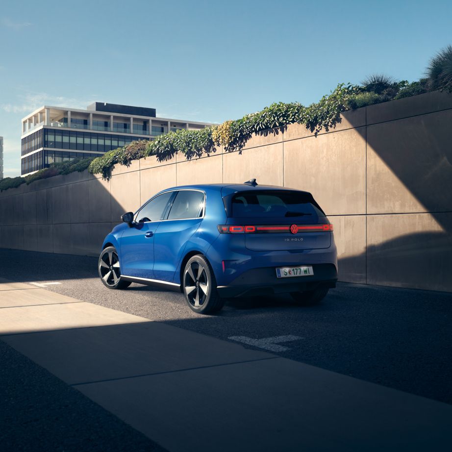 Син VW ID. Polo Style стои край пътя пред зелена стена.