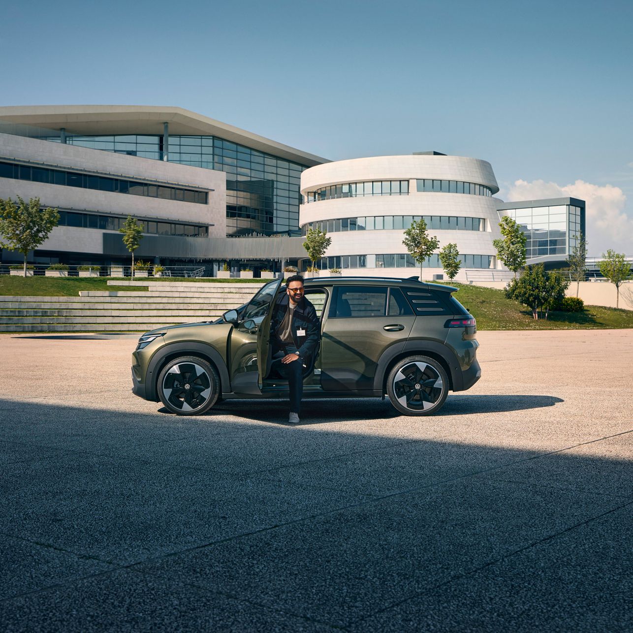 Мъж излиза през шофьорската врата на VW ID. Cross, който стои пред модерна многоетажна сграда на компанията.