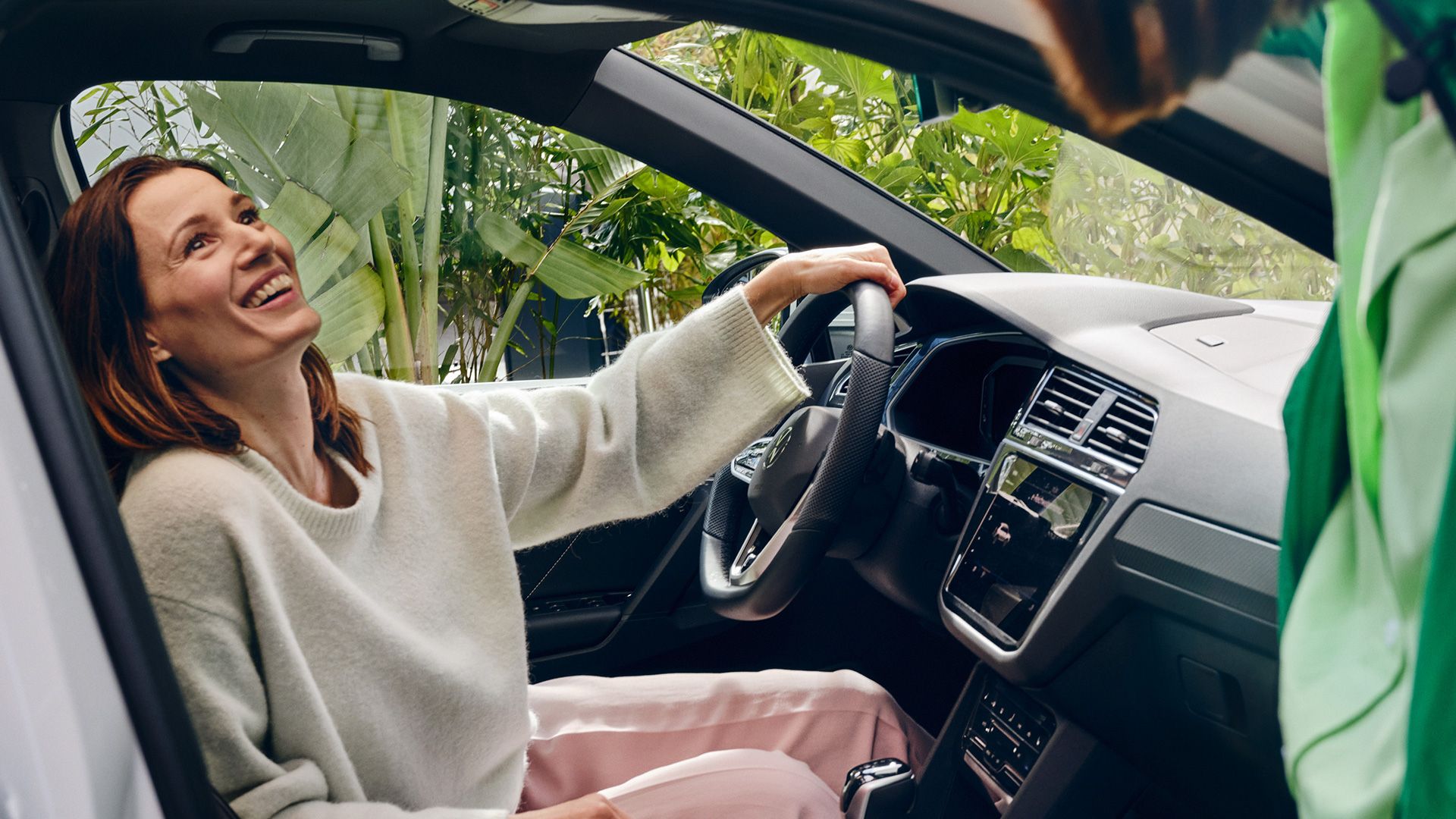 Eine lachende Frau sitzt auf dem Fahrersitz eines VW Tiguan eHybrids und hält die linke Hand am Lenkrad.