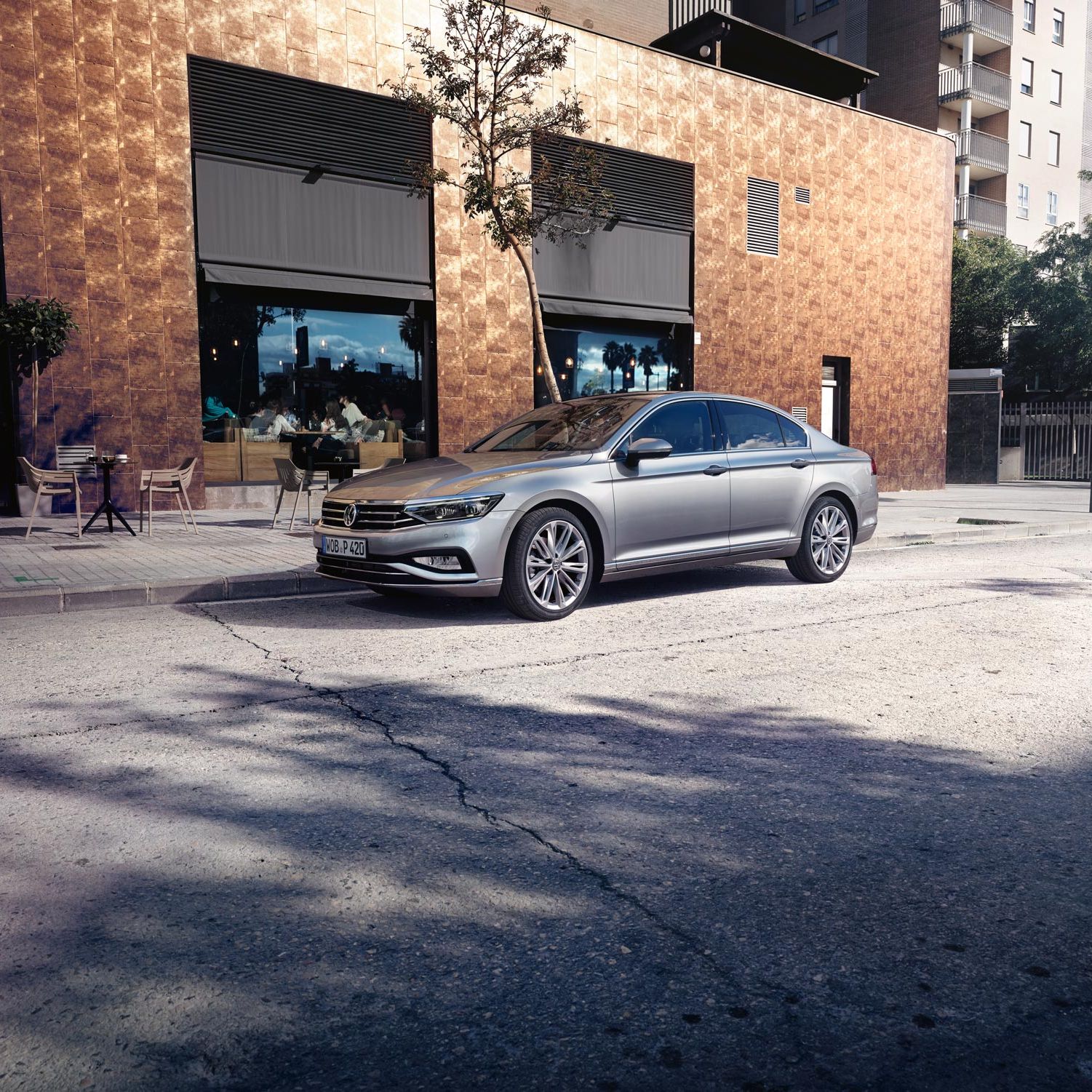 Сребрист Volkswagen Passat паркиран пред кафене в градска среда