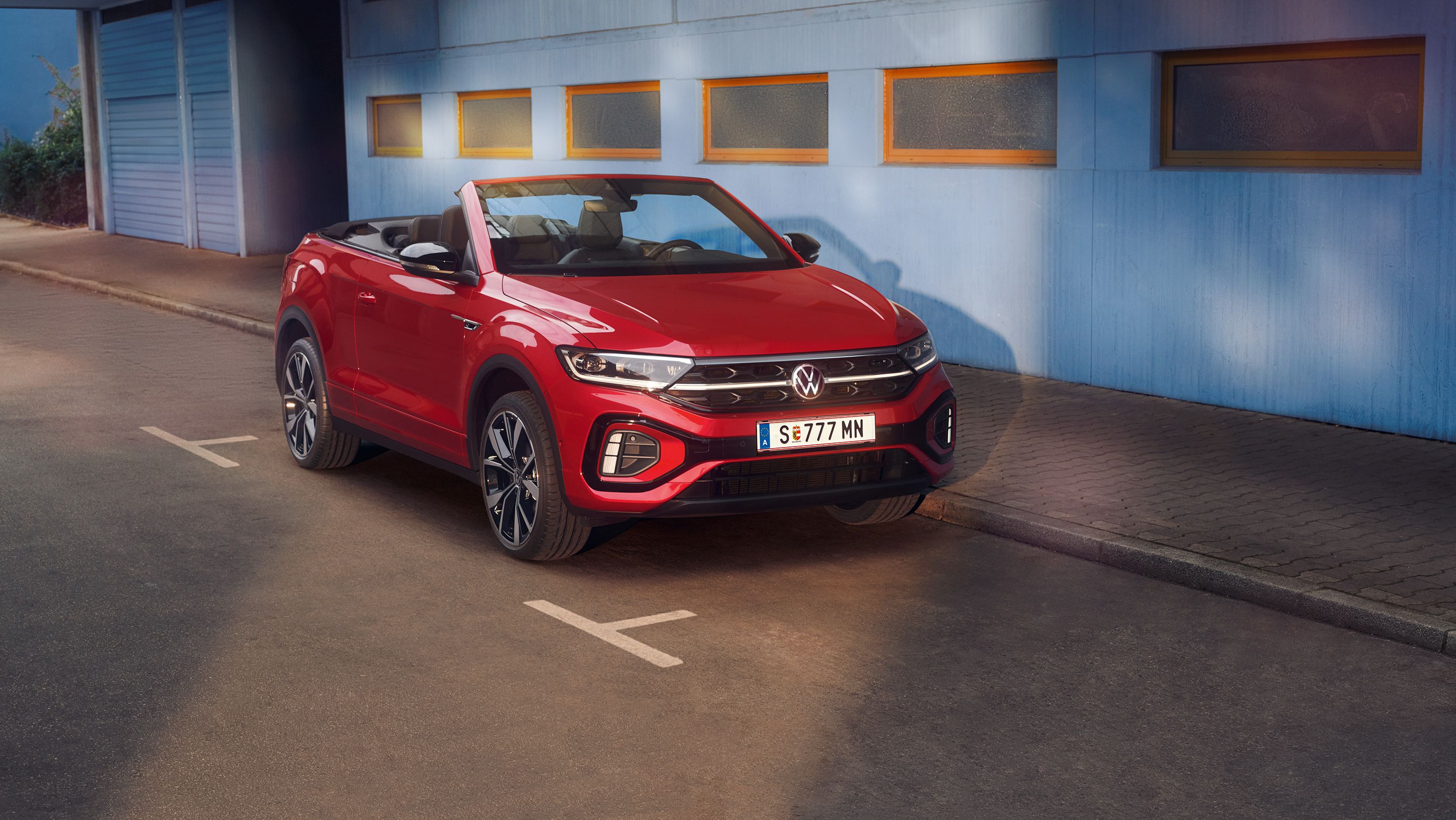 Стилен червен Volkswagen T-Roc кабриолет, заснет отпред на градска улица с отворен покрив.