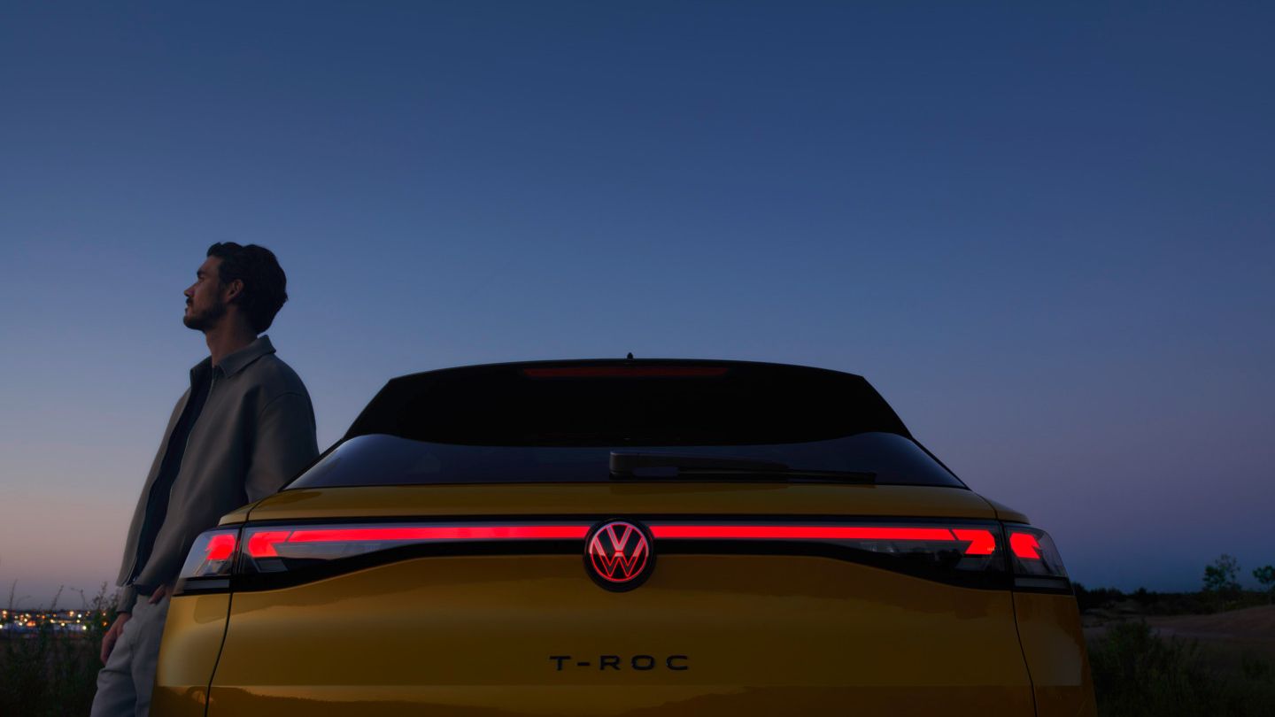 Жълт Volkswagen T-Roc с включени задни светлини под нощното небе и луната.