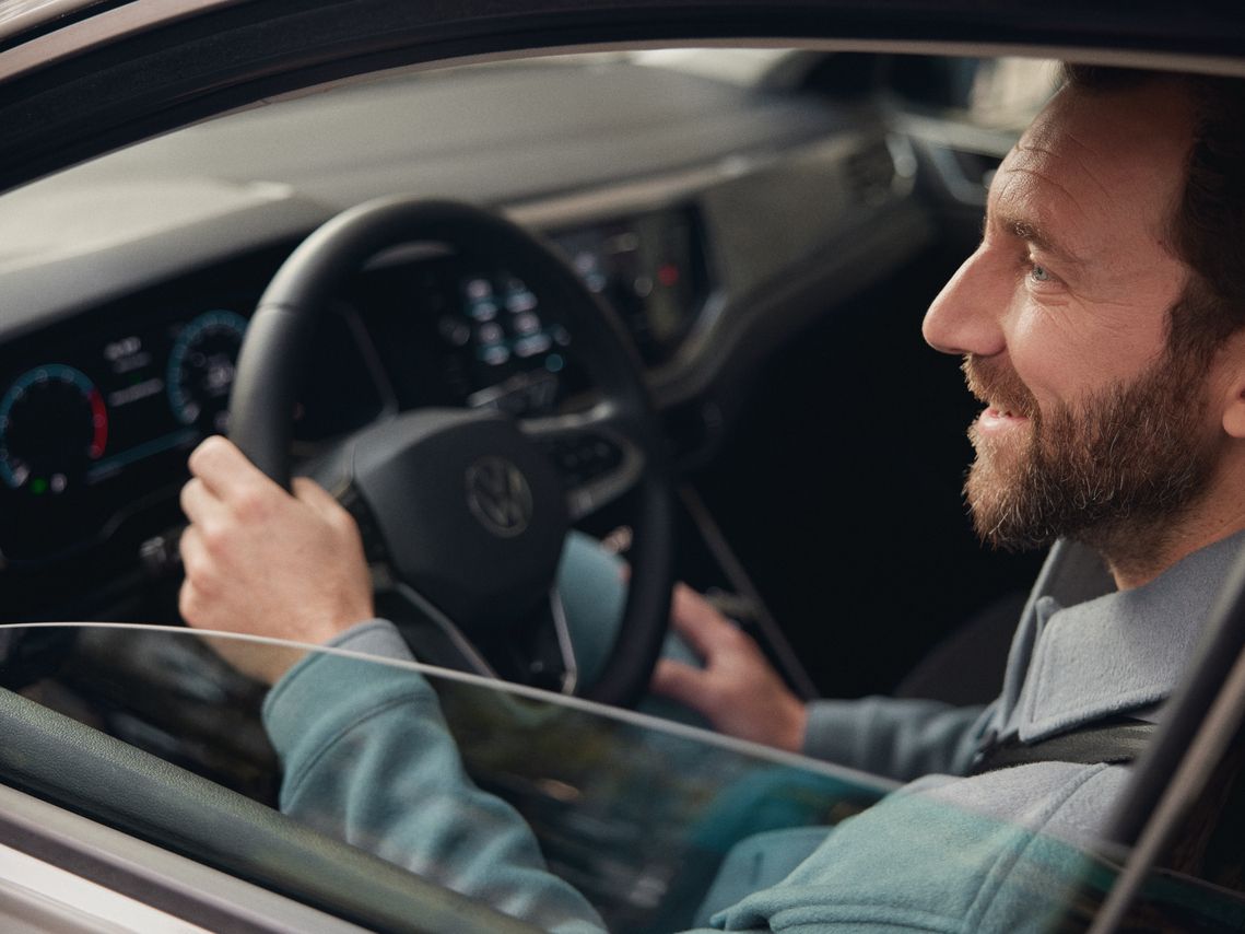 Мъж седи зад волана на Volkswagen и се усмихва
