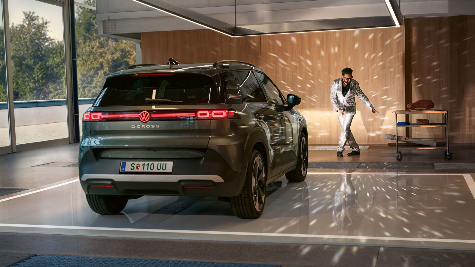VW ID. Cross стои в коридор с включени фарове и осветява танцуващ мъж в блестящ костюм.