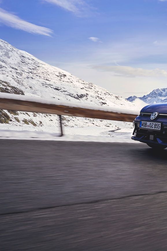 Син Volkswagen Golf R Variant с багажник на покрива, в движение по планински път сред сняг.