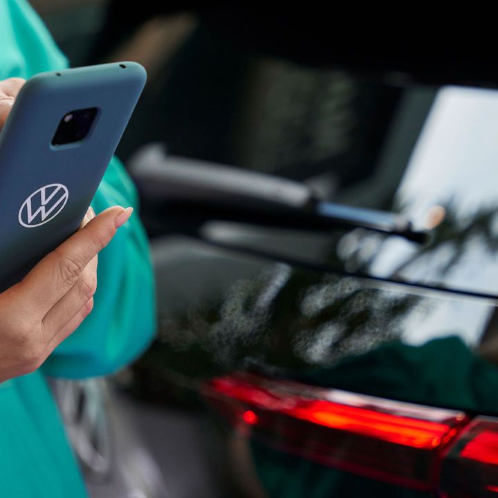 Клиент използва смартфон с калъф Volkswagen пред автомобил.