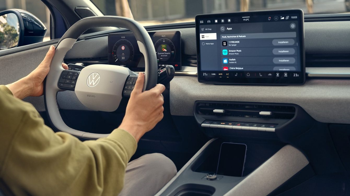 Млад мъж шофира модерен електрически автомобил Volkswagen ID.Polo, гледан от вътрешността на купето. На таблото пред него има голям централен сензорен екран с интерфейс за навигация и медии. През прозорците се виждат модерни градски сгради и зелени дървета.