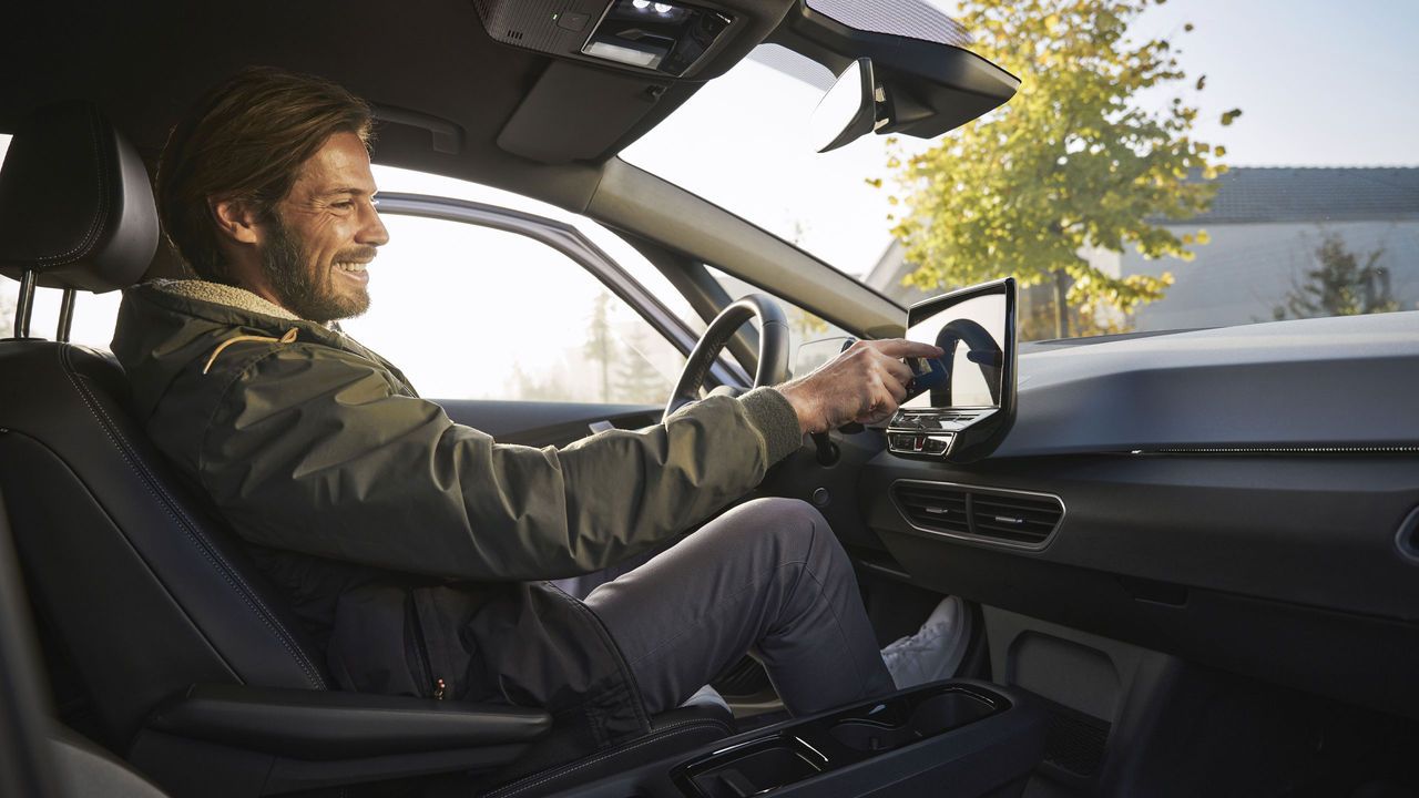 Усмихнат мъж седи на седалката на водача на автомобил и манипулира с инфотеймънт системата