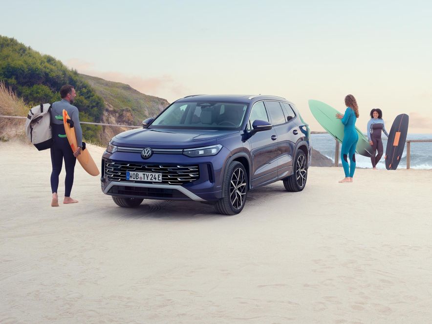 Volkswagen Tayron паркиран на плажа, докато сърфисти се подготвят за морското приключение