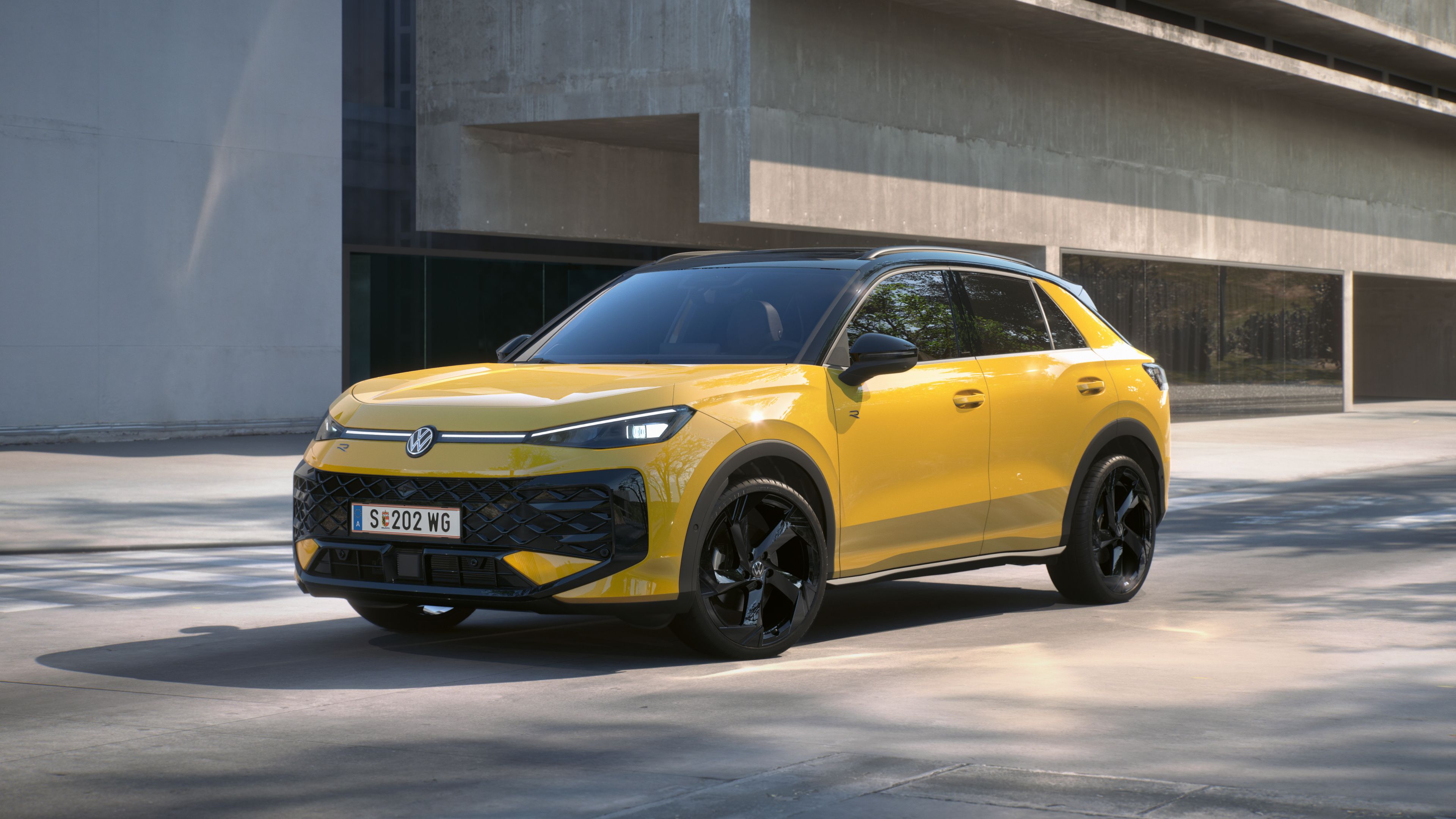 Жълт Volkswagen T-Roc R-Line паркиран пред модерна бетонна сграда.