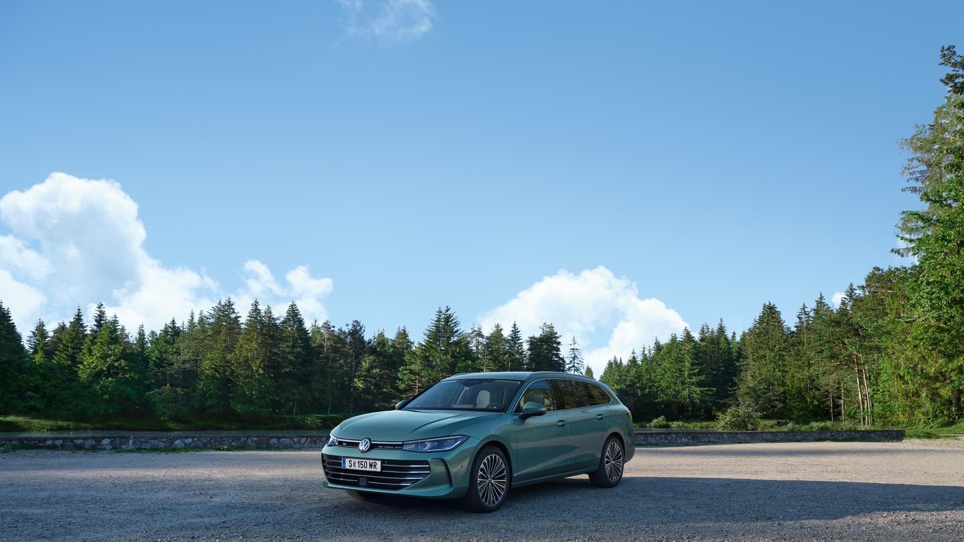 VW Passat в синьо-зелен цвят е спрял върху чакълест терен, местността граничи с елхова гора.