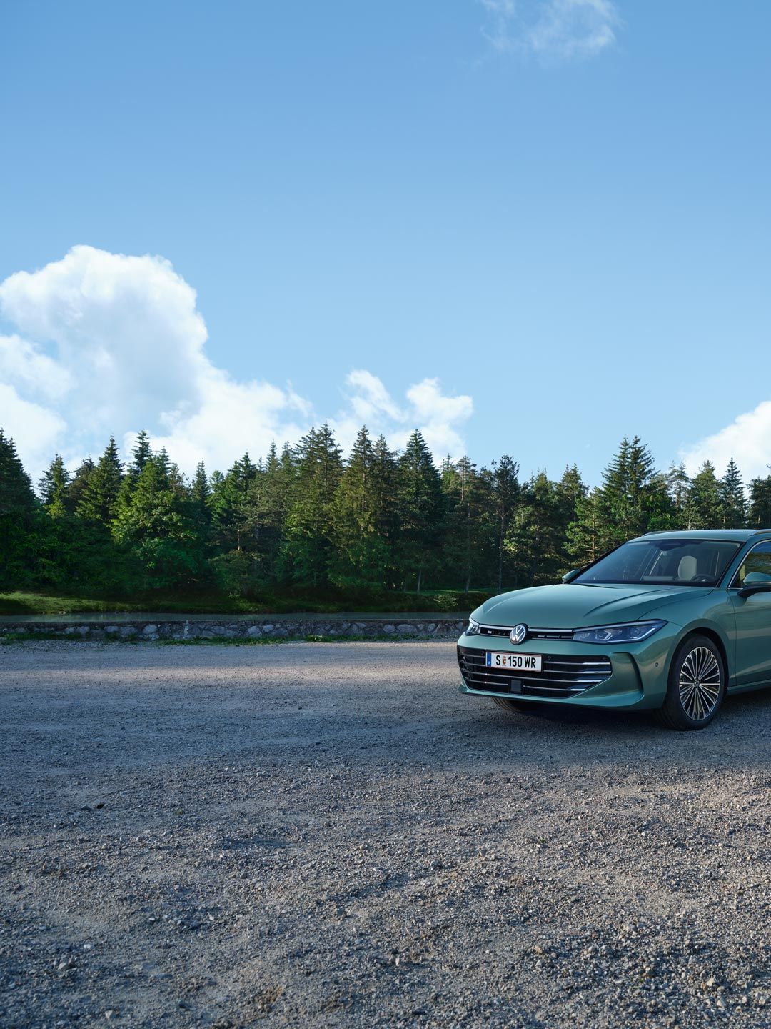 VW Passat в синьо-зелен цвят е спрял върху чакълест терен, местността граничи с елхова гора.