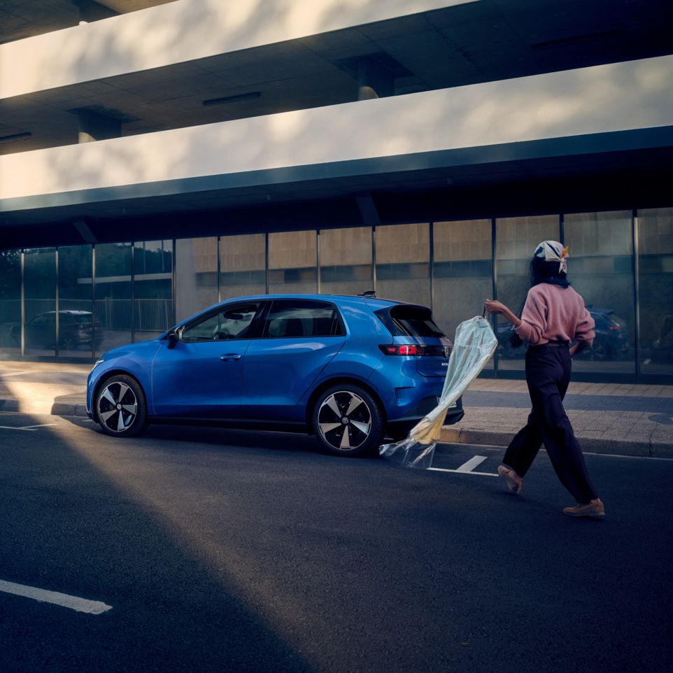 Син VW ID. Polo Style е паркиран край пътя, жена се приближава към автомобила.