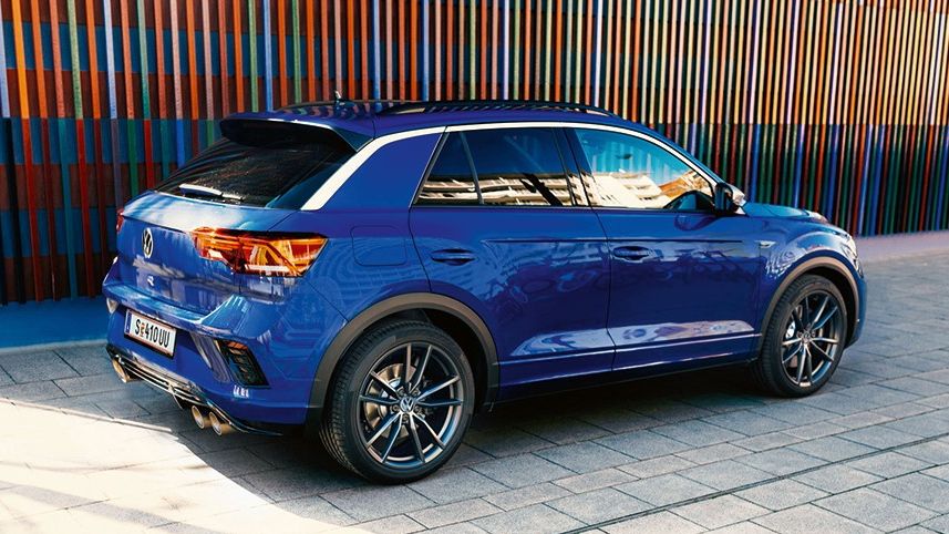 Син Volkswagen T-Roc R, паркиран пред стена с цветни вертикални панели в градска среда.