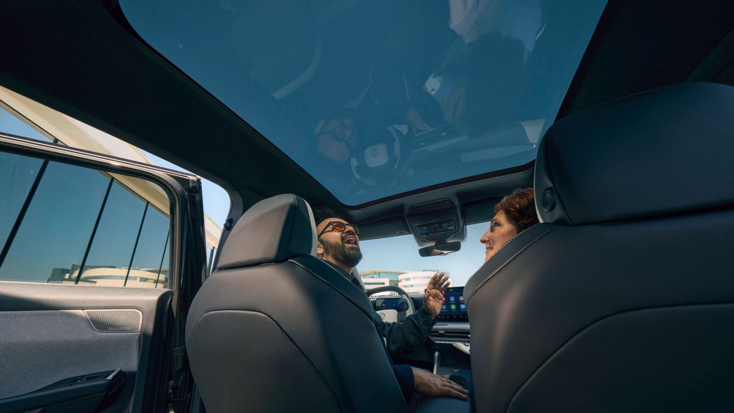 Усмихнат мъж седи на шофьорската седалка на VW ID. Cross и гледа през отворения панорамен покрив.