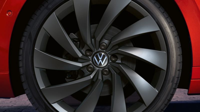 Близък план на тъмносивa алуминиева джанта с емблема Volkswagen на червен Arteon Shooting Brake