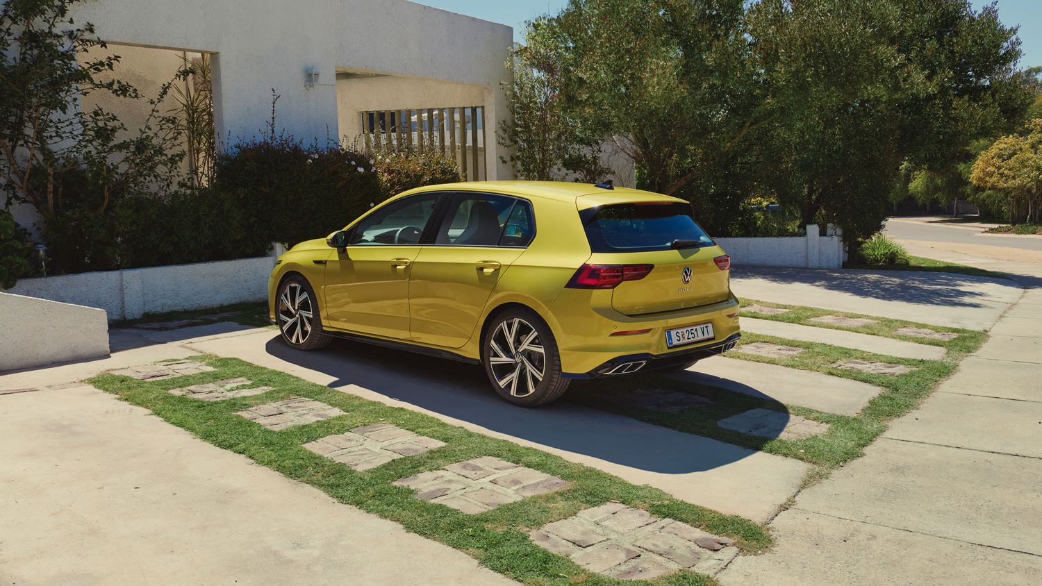 Жълт Volkswagen Golf, паркиран пред модерна сграда сред зеленина и естествена светлина