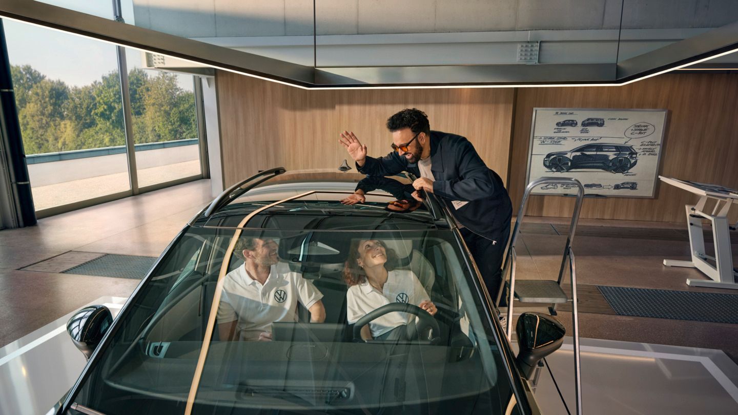 Мъж стои на стълба до VW ID. Cross и маха през панорамния покрив на хората, които седят вътре в автомобила.