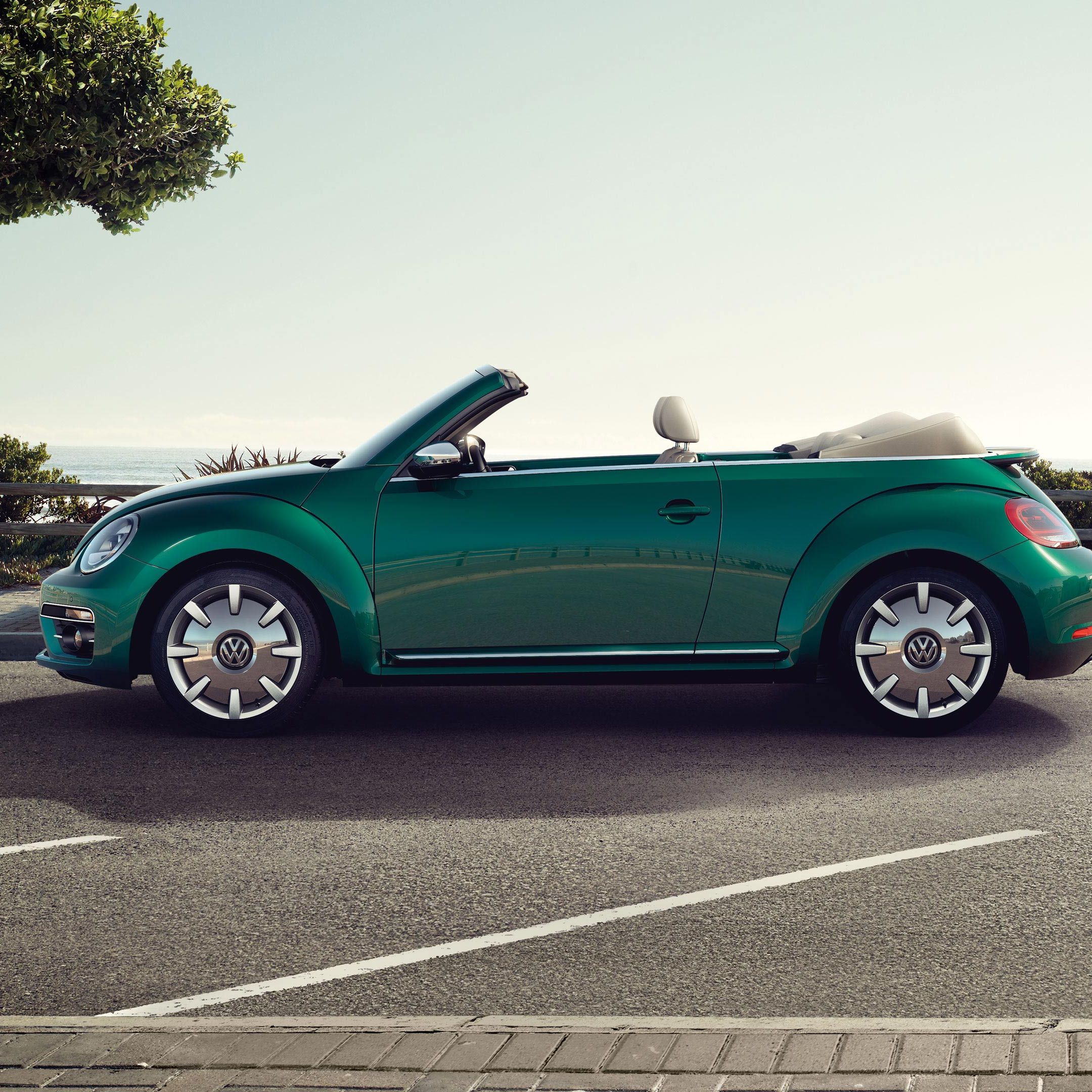 Стилен зелен Volkswagen Beetle Cabriolet паркиран до крайбрежна улица с изглед към морето
