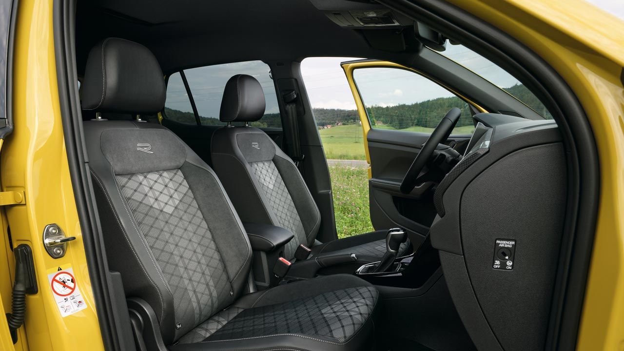 „Поглед през пътническата врата на жълт VW T-Cross с допълнително предлаганите спортни комфортни седалки и централния подлакътник.“