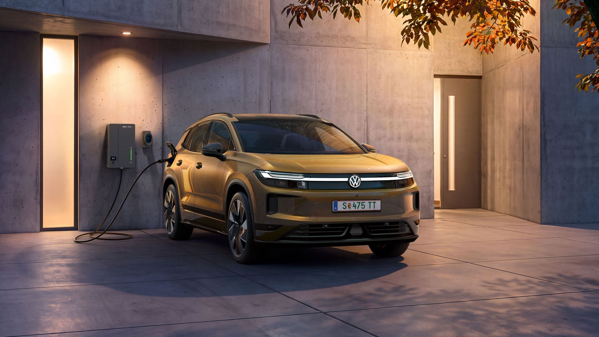 Ein oliv-bronzefarbener VW ID.Tiguan Style steht vor einem modernen Haus in der Abenddämmerung an einer Elli Bi-Di Wallbox.